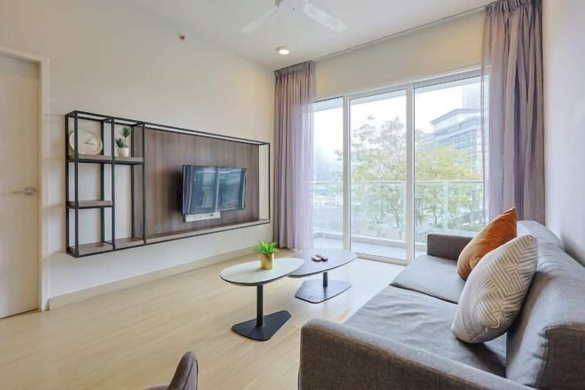 A modern living room with a sofa, a coffee table, a TV mounted on a wall, and a balcony with curtains.