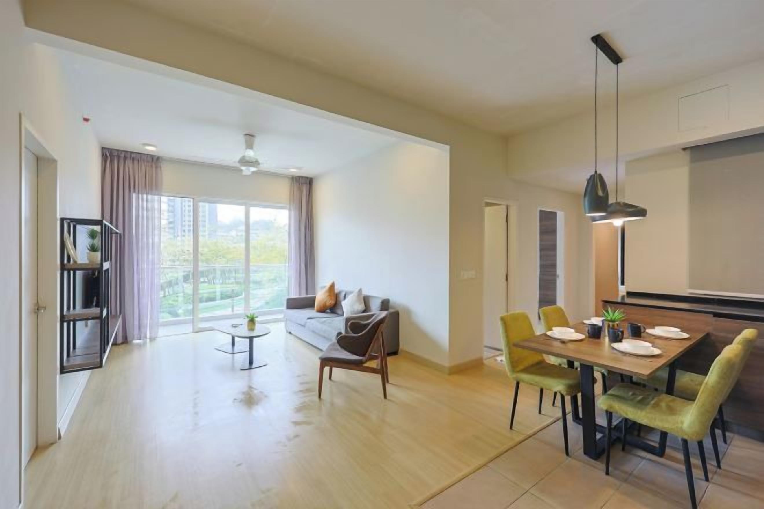 A spacious living area with a sofa, dining table, and chairs, a bookshelf, and a large window with curtains.