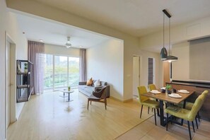 Amplia sala de estar con sofá, mesa de comedor y sillas, una estantería y un ventanal con cortinas.