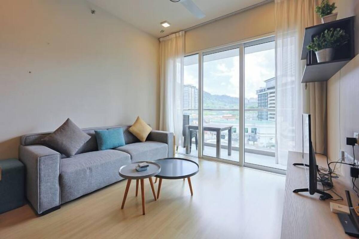 A modern living room with a sofa, two side tables, a flat-screen TV, and a large window with a city view.