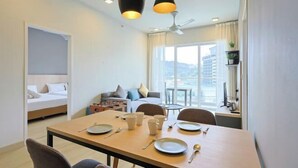 A hotel room with a dining area, a bed, a sofa, a desk, and a balcony with a view.