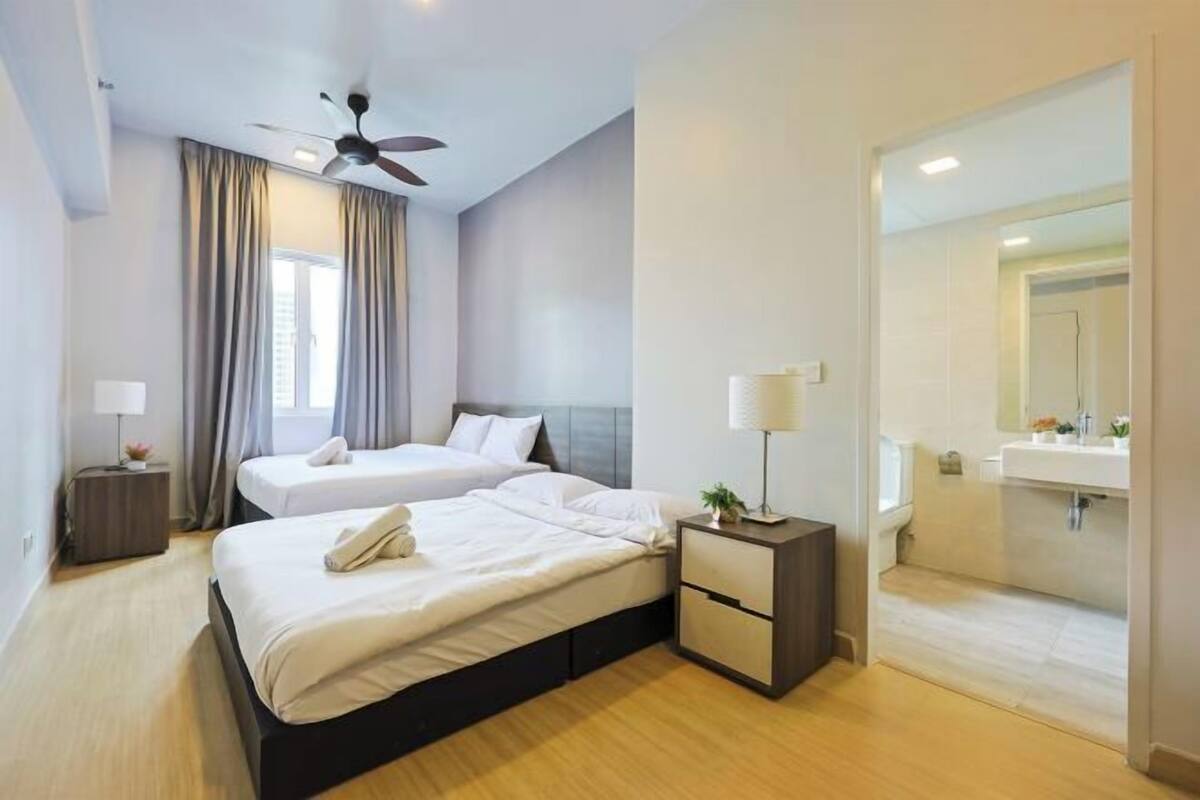 A modern hotel room with two beds, a ceiling fan, a bedside table with a lamp, and a view of the bathroom.