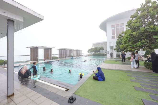 A rooftop pool area with people swimming and sitting on the grass.