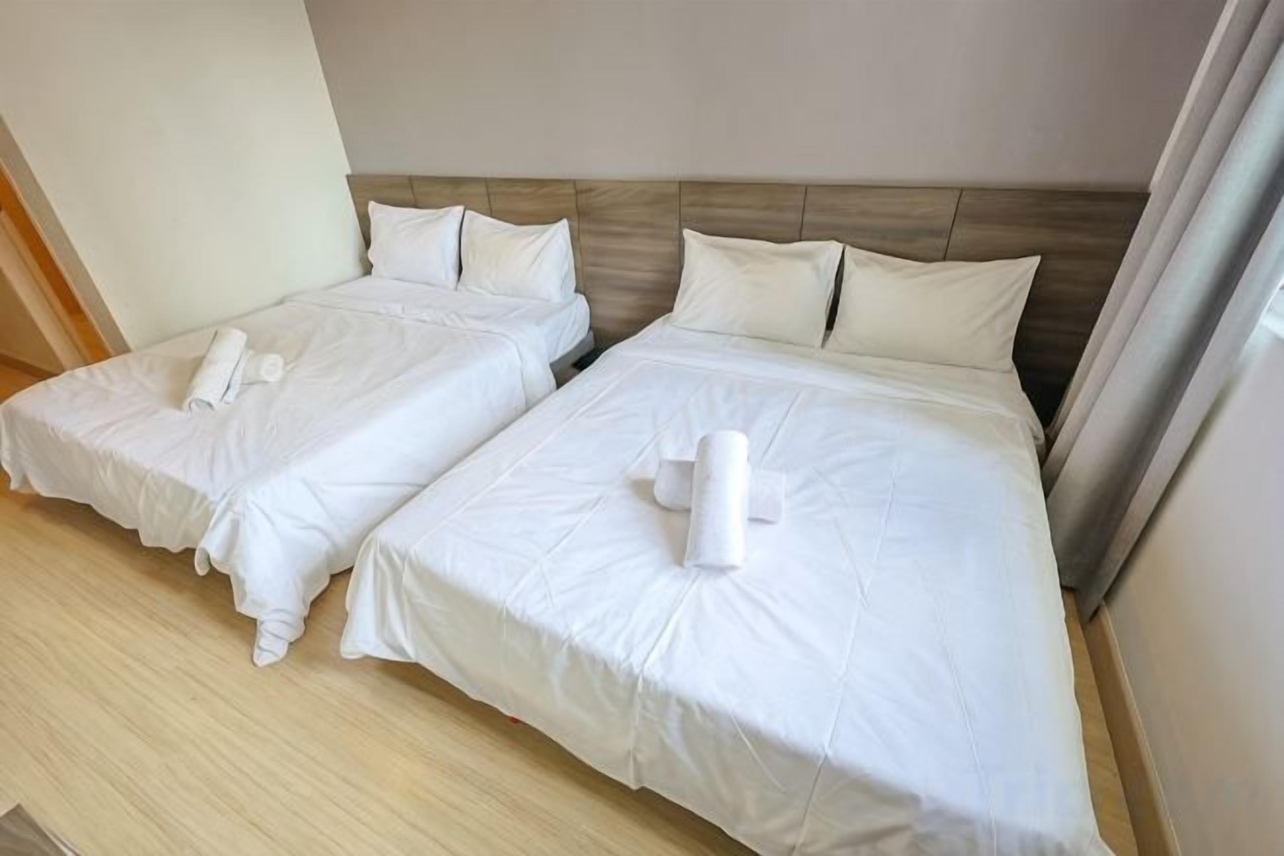 Two single beds with white linens and towels, a wooden headboard, and a neutral-colored wall.