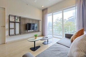 Un salon moderne avec un téléviseur à écran plat, une petite table sur laquelle est posée une plante, un canapé et une grande fenêtre donnant sur des immeubles.