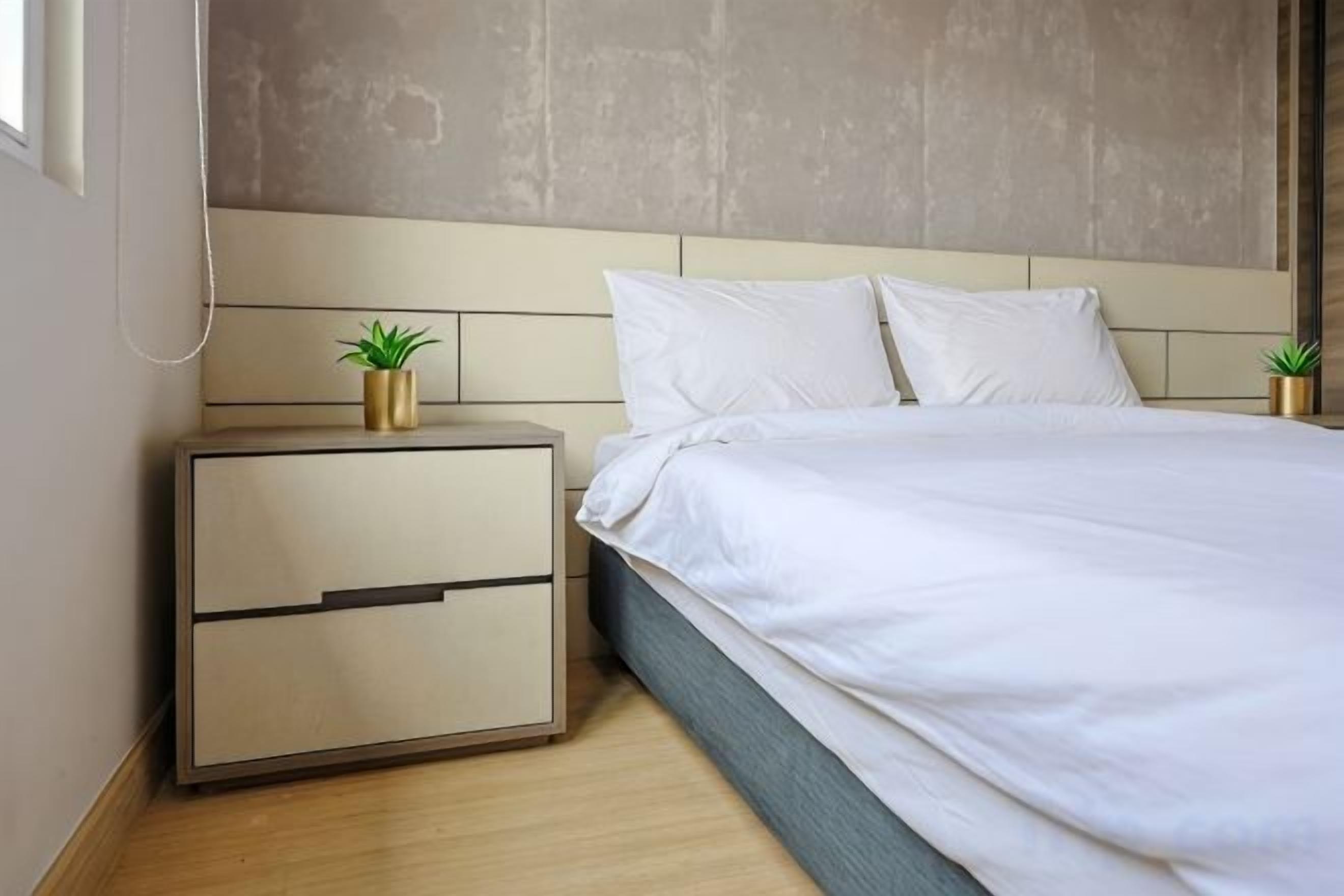 A bedroom with a bed, nightstand, and a wall-mounted plant.