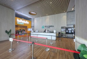Un espace d’accueil avec un plancher en bois, une barrière en corde rouge et un comptoir sur lequel est affiché un panneau indiquant « bilabita mart ».