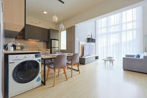 A modern kitchen with a washing machine, dining area with chairs, and a large window with curtains.