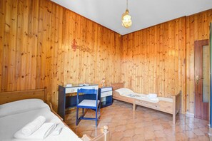 Une pièce aux murs en bois, avec un lit, un bureau et une chaise, ainsi qu’une petite table de chevet.