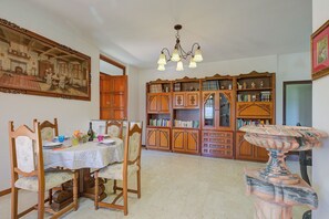 Un coin repas avec une table dressée pour quatre personnes, entourée de chaises en bois, d’un lustre et d’une bibliothèque remplie de livres.
