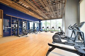 A gym with exercise equipment, large windows, and a wooden floor.