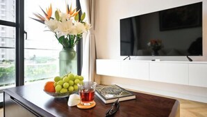 Un salon moderne avec une table basse en bois, un vase rempli de fleurs, un saladier de fruits, une tasse de thé et un livre.