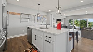 A modern kitchen with white cabinetry, a central island, stainless steel appliances, and pendant lighting. - Modern 3BR with Breathtaking Skyline Views (Pittsburgh)