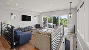 A spacious living area with a sofa, a TV, and a balcony with a railing. - Modern 3BR with Breathtaking Skyline Views (Pittsburgh)