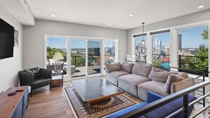 A spacious living room with a large sofa, a coffee table, and a TV. - Modern 3BR with Breathtaking Skyline Views (Pittsburgh)