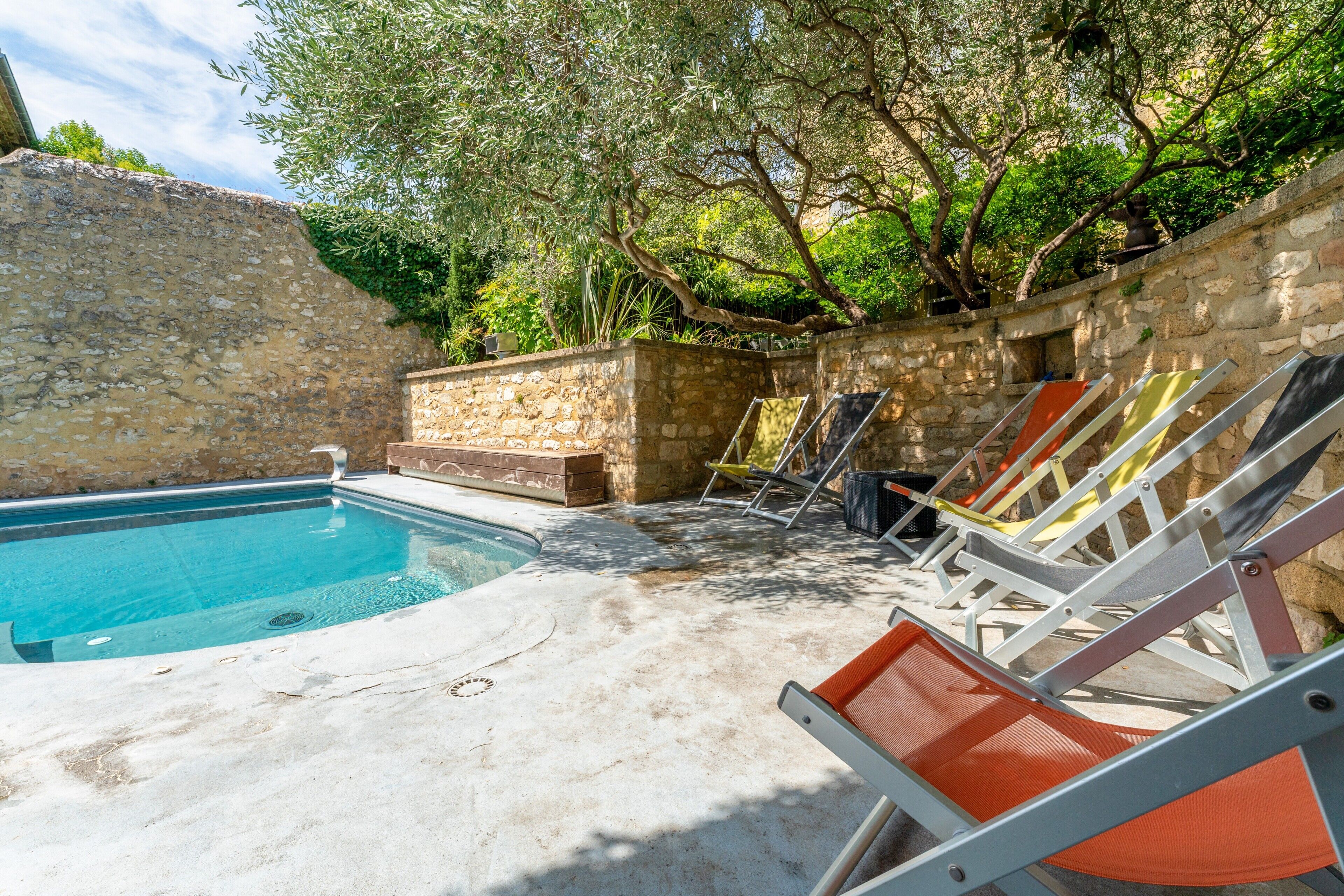 A swimming pool with lounge chairs, a stone wall, and greenery.