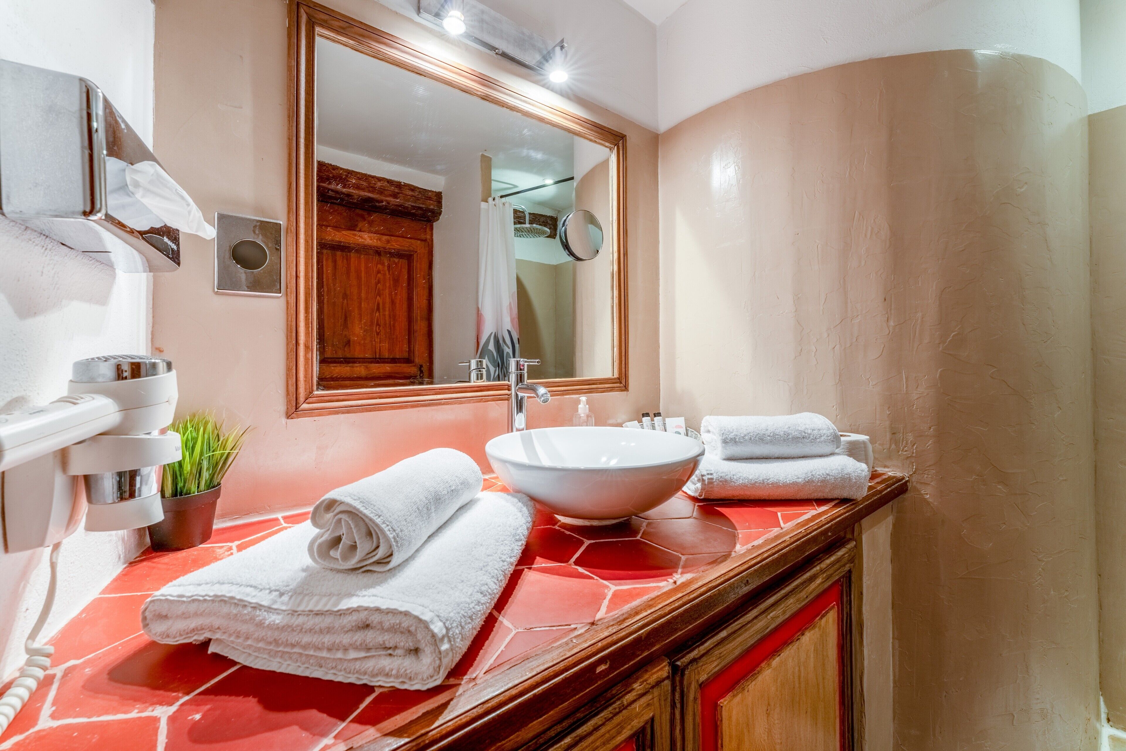 A bathroom with a large mirror, a white sink, and a red-tiled countertop.