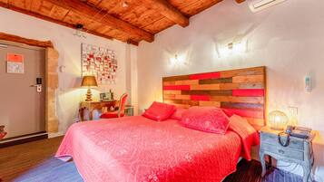 Une chambre avec un plafond en bois, un lit recouvert d’une couverture rouge, une table de chevet avec une lampe et un mur orné d’un tableau d’affichage.