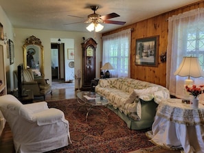 A traditional living room with a sofa, armchair, and a coffee table. A grandfather clock and a ceiling fan are visible. - Hot Tub + Fishing Pond + King Suite Retreat (8-10) (Thomas)