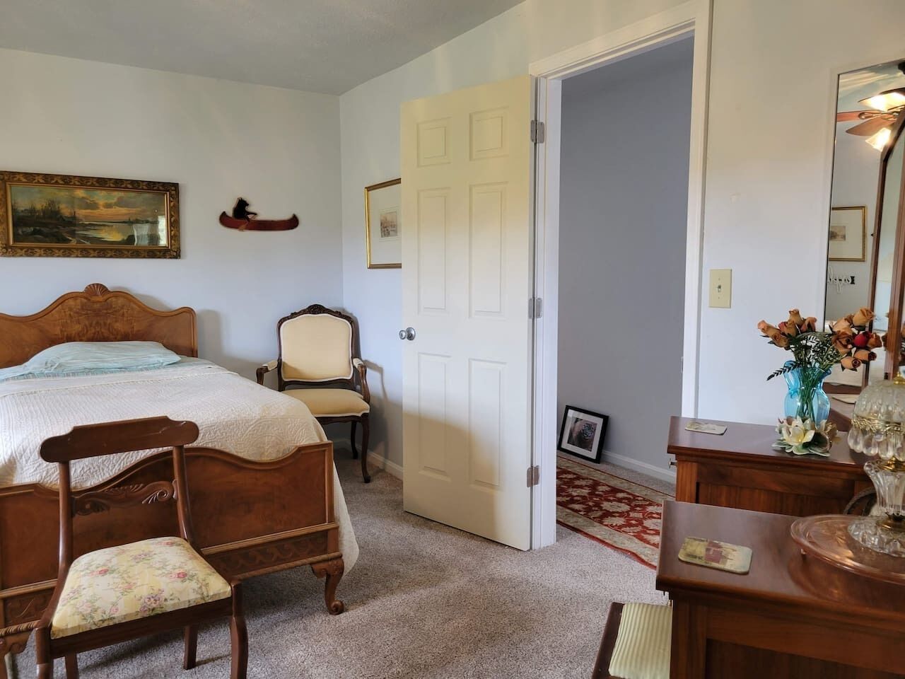 A bedroom with a bed, two chairs, a dresser, a door, and a painting on the wall.