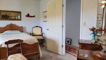 A bedroom with a bed, two chairs, a dresser, a door, and a painting on the wall.