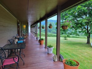 A covered outdoor seating area with tables and chairs, potted plants, and a view of a grassy landscape. - Hot Tub + Fishing Pond + King Suite Retreat (8-10) (Thomas)