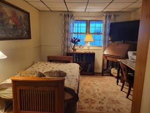 A bedroom with a bed, a desk, a lamp, a TV, and a window with curtains.