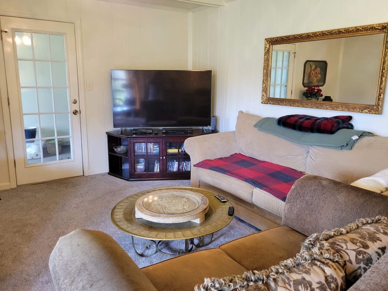 A living room with a flat-screen TV, a sofa with a plaid blanket, a coffee table, and a bookshelf.