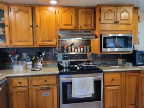 A kitchen with wooden cabinets, a stainless steel microwave, a stove, and various kitchen utensils.
