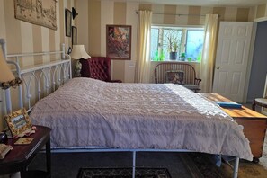 A bedroom with a bed, a chair, a desk, a window with curtains, and a door.
