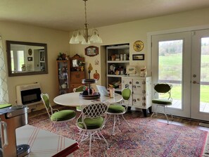 A dining area with a round table, green cushioned chairs, a chandelier, and a view through a glass door.