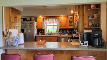 A kitchen with wooden cabinets, a refrigerator, a coffee maker, and a window with curtains.