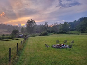 A grassy field with a circular seating area and chairs, surrounded by a fence and trees. - Hot Tub + Fishing Pond + King Suite Retreat (8-10) (Thomas)
