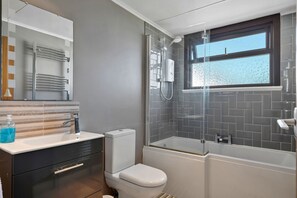 Ett modernt badrum med en dusch som är avskärmad med glasväggar, en vit toalett och ett handfat med en spegel ovanför.