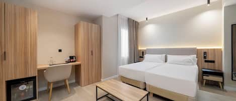 A modern hotel room with a bed, a desk, and a seating area.