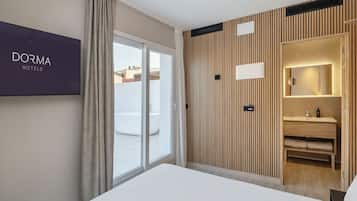 Moderni hotellihuone, jossa on suuri sänky, lasiliukuovi parvekkeelle, puupanelilla verhoiltu seinä ja seinälle asennettu televisio, jossa näkyy teksti ’DORMA HOTELS’.