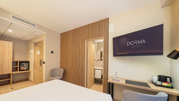 Una habitación de hotel con cama, escritorio, silla, televisor y minibar.