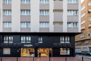 Un hotel moderno con fachada negra, múltiples ventanas y una tienda visible llamada 'GAUDEA' en la planta baja.