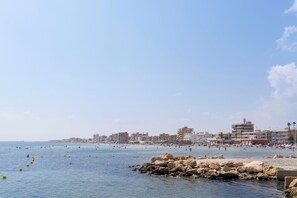 A coastal cityscape with a beach, rocky shoreline, and buildings in the background. - Dorma Gaudea Santa Pola (Santa Pola)