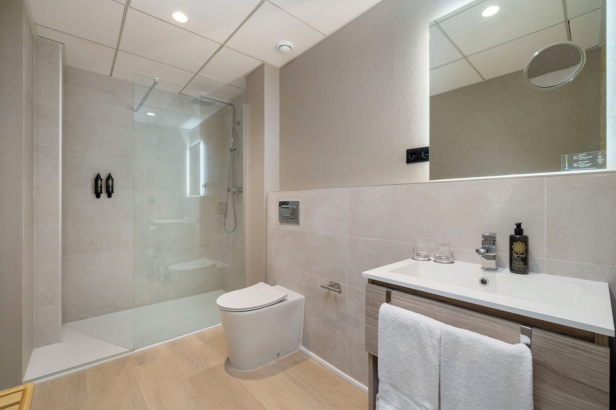 Un baño moderno con ducha envuelta en vidrio, un inodoro blanco, un tocador con espejo y un perchero para toallas.