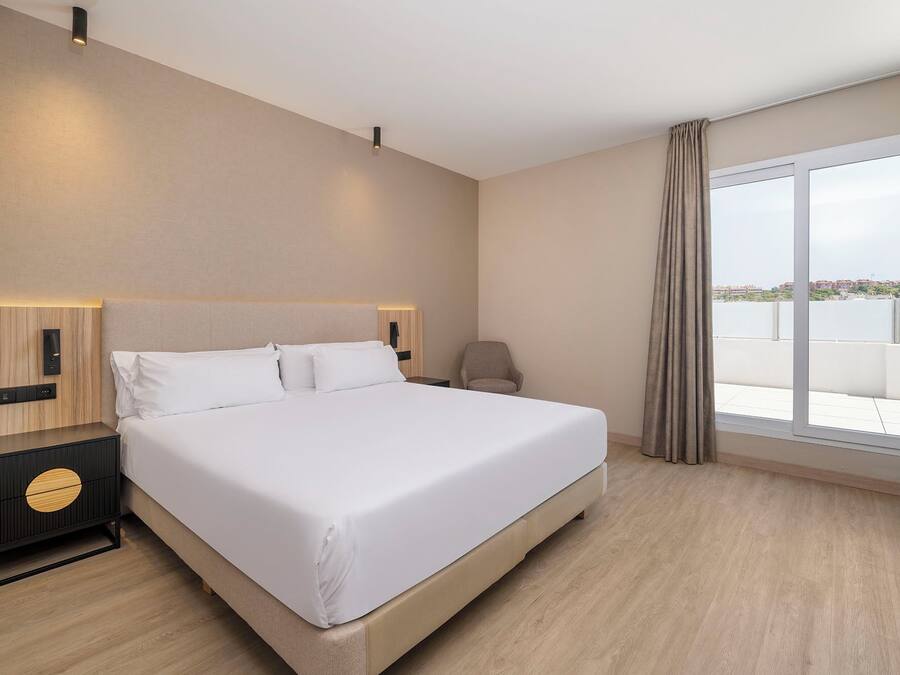Ein Hotelzimmer mit einem großen Bett, Nachttischen, einem Sessel und Blick auf die Stadt.