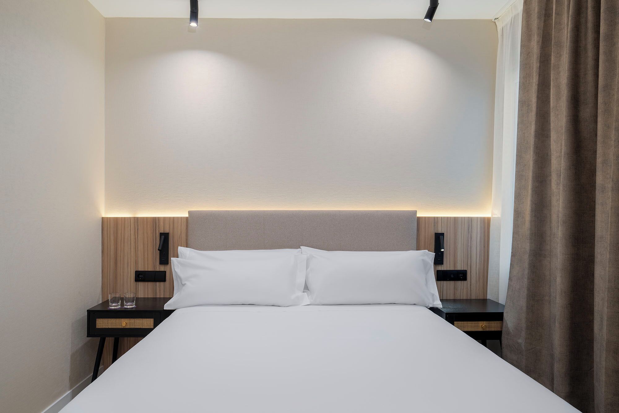 Ein Hotelzimmer mit einem Bett, Nachttischen und einem Kopfteil mit integrierter Beleuchtung.