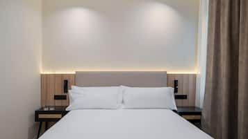 Habitación de hotel con cama, mesitas de noche y cabecera con iluminación integrada.