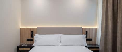A hotel room with a bed, bedside tables, and a headboard with integrated lighting.