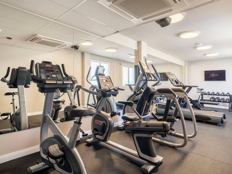 A gym with various cardio machines, a wall-mounted mirror, and a sign indicating a hotel.