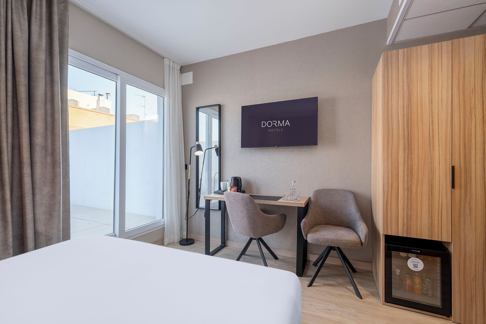 A hotel room with a bed, a desk with two chairs, a television, and a minibar.