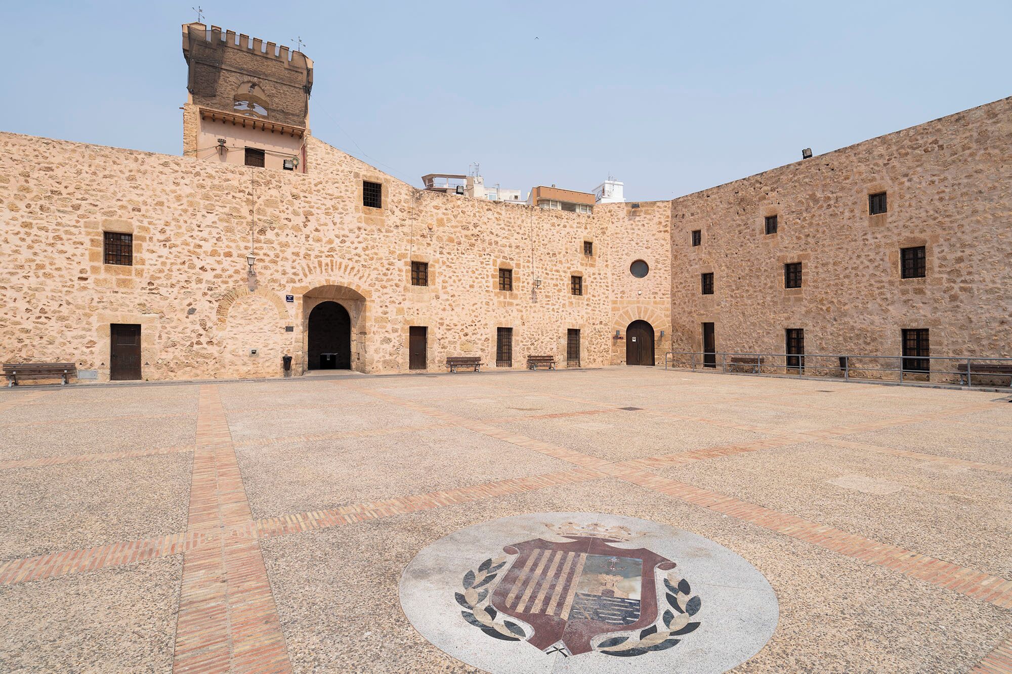 Un patio con un edificio de piedra que cuenta con varios arcos y un emblema central.