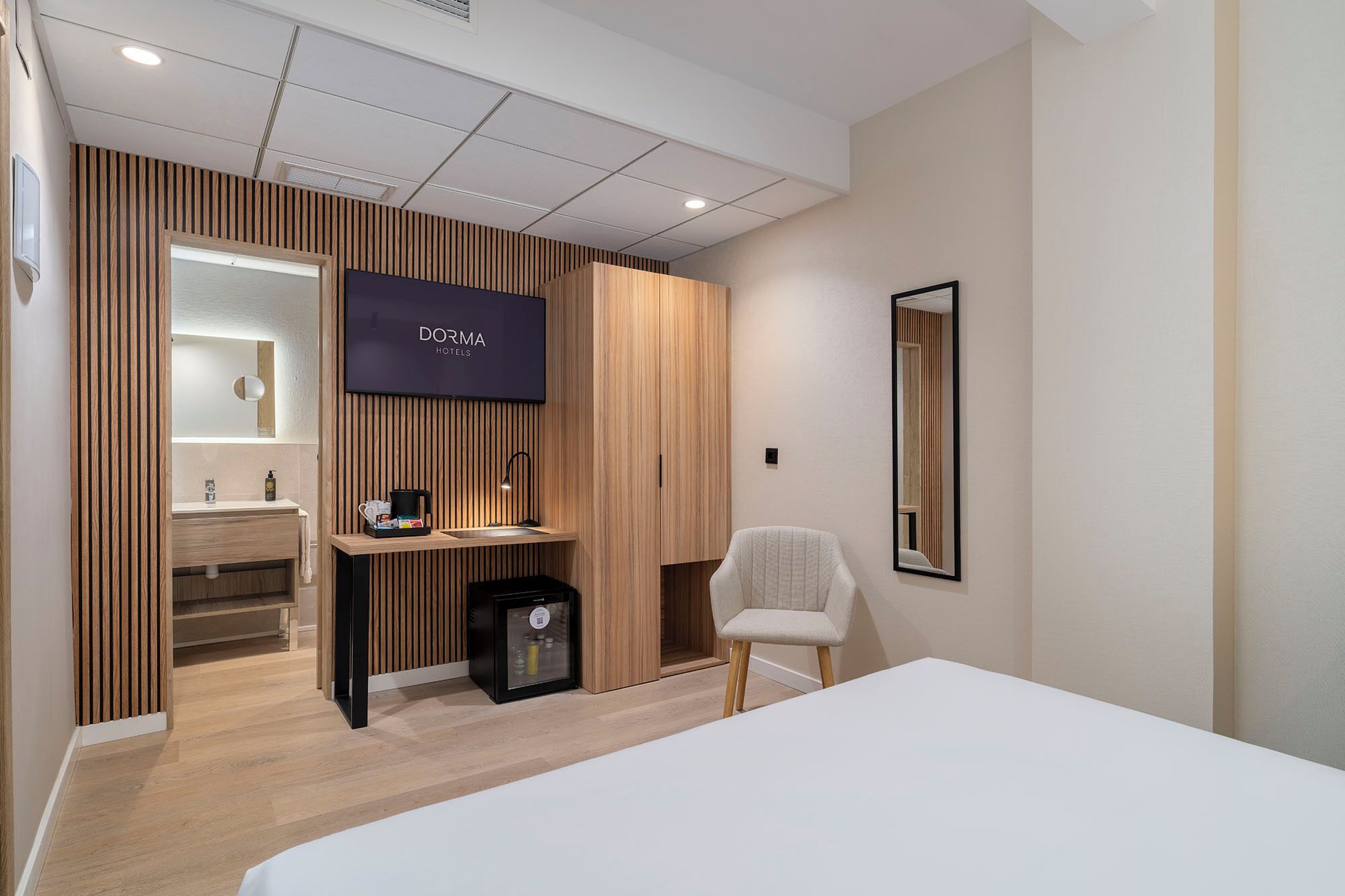Una camera d'albergo moderna con un letto, una scrivania con un computer, una sedia, una televisione e un armadio.