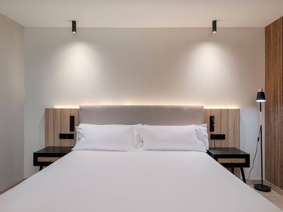 Habitación de hotel moderna con una cama grande, dos mesitas de noche y una lámpara de pie.