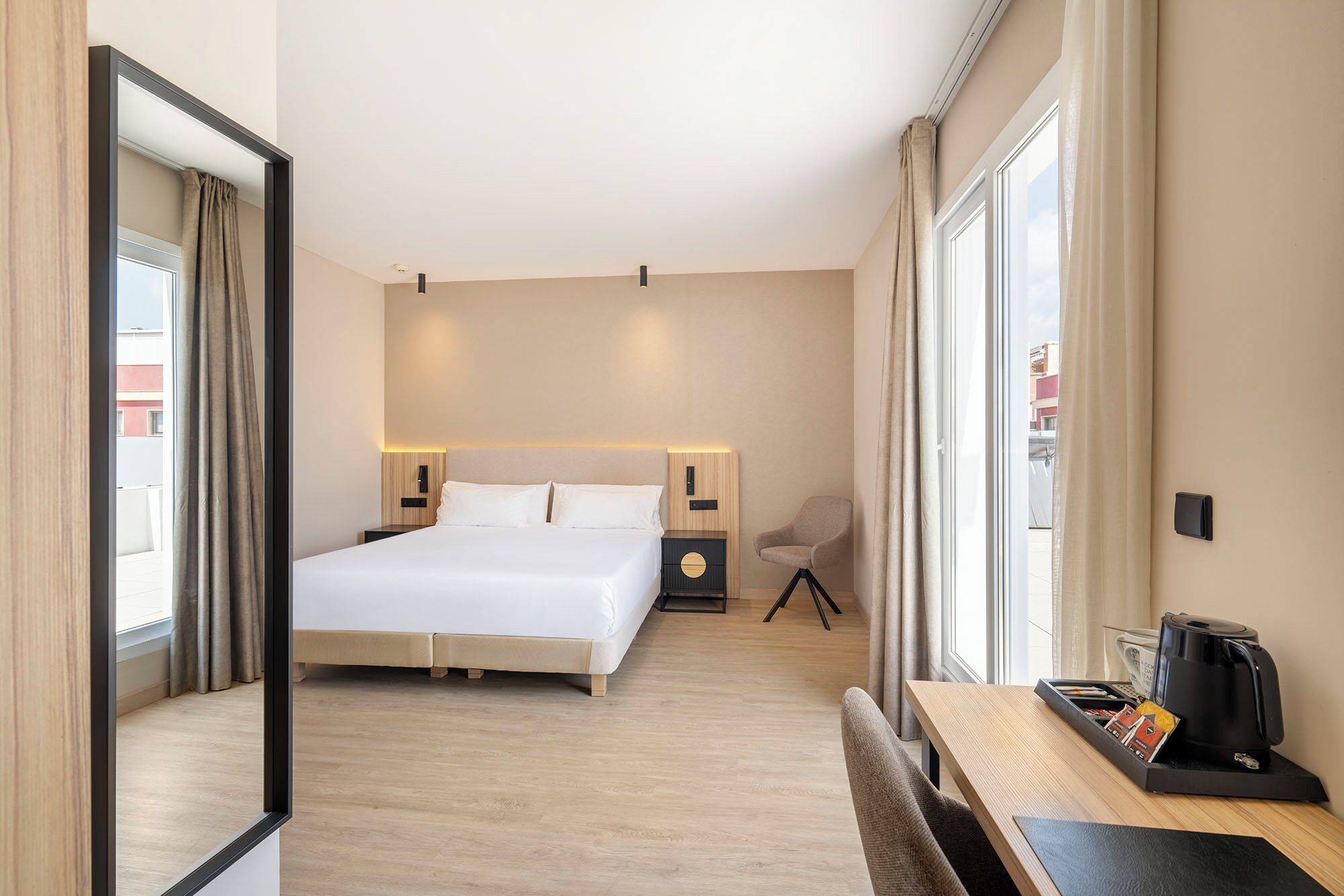 A hotel room with a large bed, bedside tables, a chair, a desk with a coffee maker, and a view through the window.